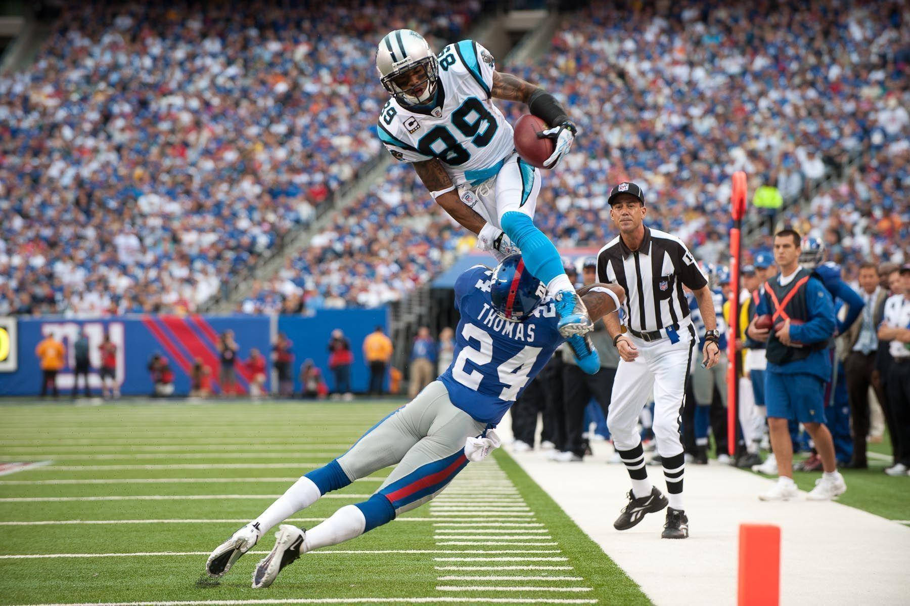 NFL球員激烈對抗 壁紙 — 一名美式足球員跳過一名潛水的防守球員，在擁擠的體育館比賽中於端區附近接住球。
