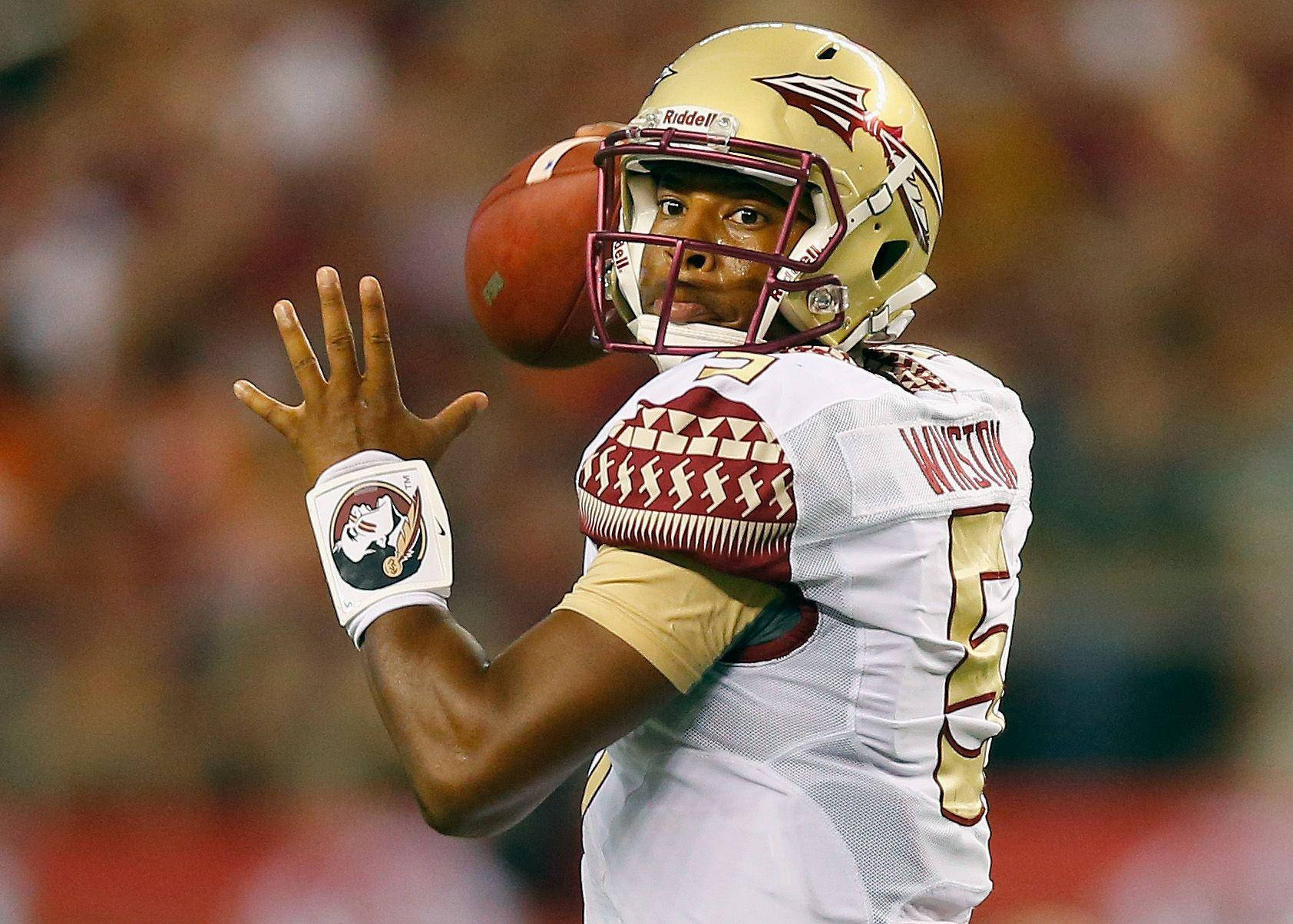NFL球員賈梅斯·溫斯頓攝影賽 壁紙 — 一名穿著佛羅里達州立大學球衣的美式足球四分衛在球場燈光下準備傳球。
