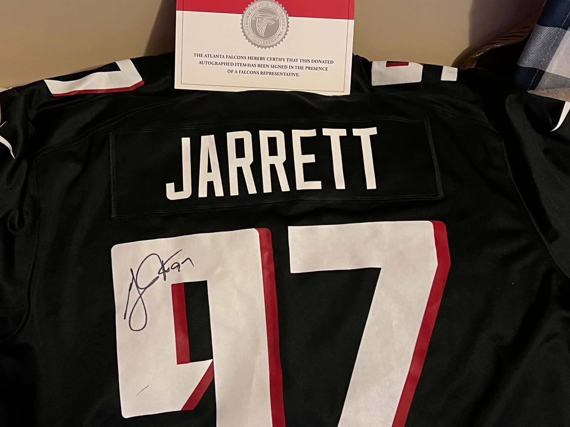 NFL球星格雷迪·賈雷特親筆簽名球衣 壁紙 — 一件帶有 'JARRETT' 和 97 號的簽名黑色亞特蘭大獵鷹球衣，附有認證證書。