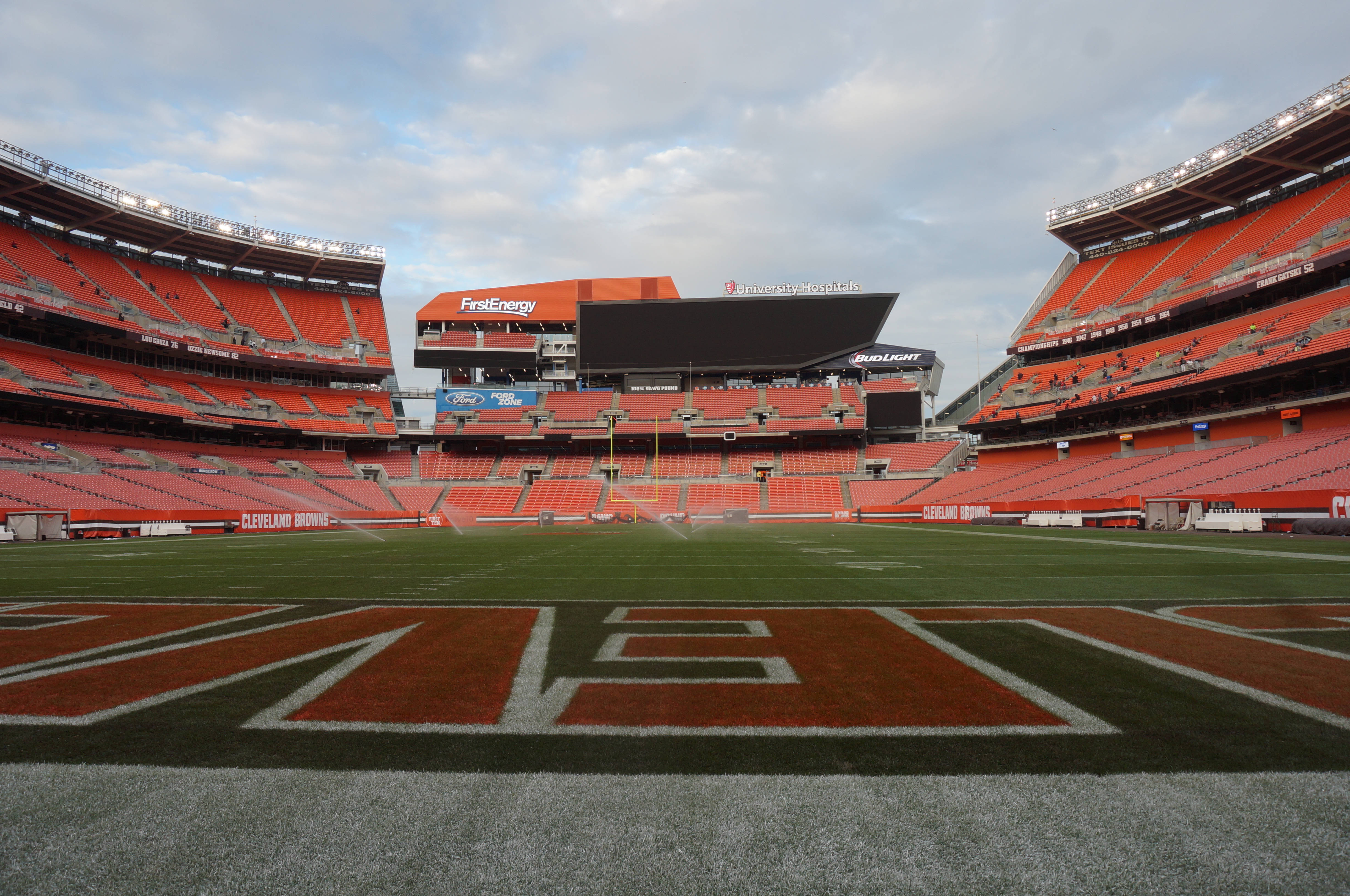 NFL美式足球場 壁紙 — 一個空無一人的克里夫蘭布朗體育場，設有橙色座位和綠色球場，天空多雲。