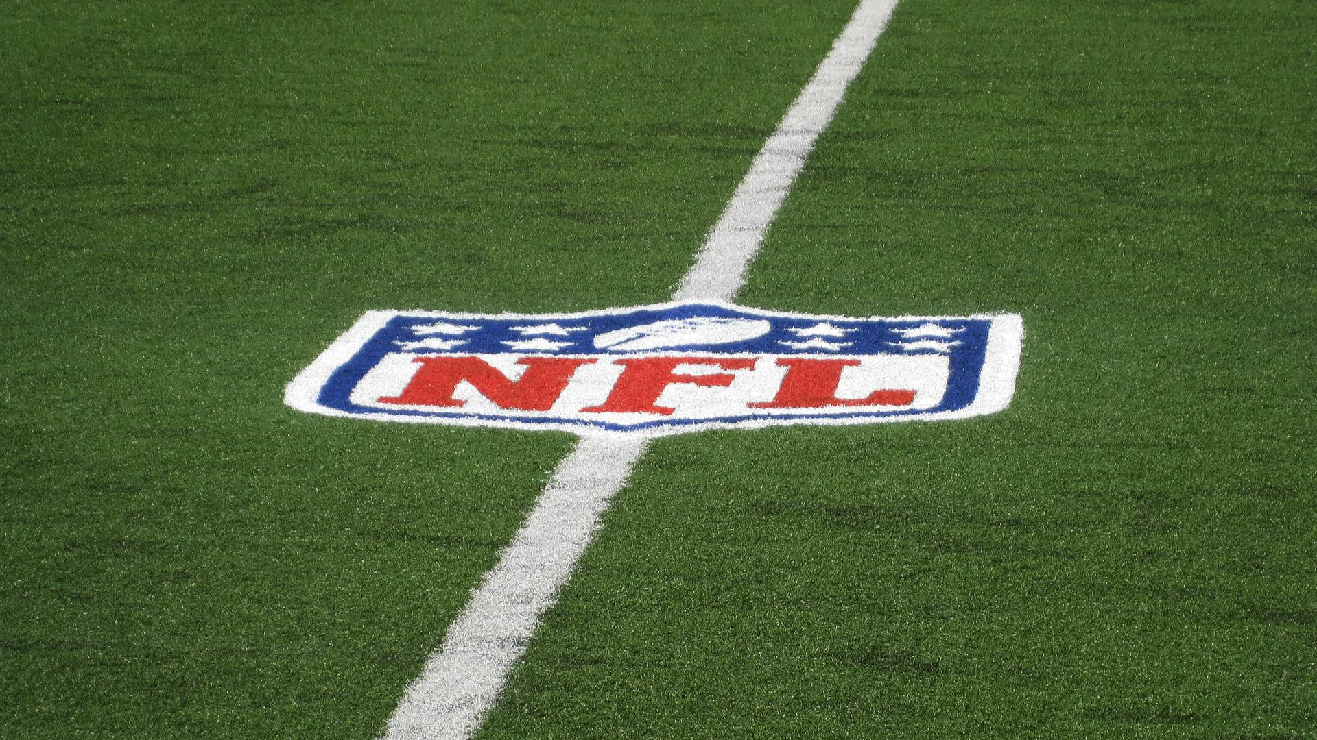 NFL美式足球場上的隊徽 壁紙 — NFL標誌的特寫，塗在充滿活力的綠色草地上，有一條清晰的白色碼線穿過。