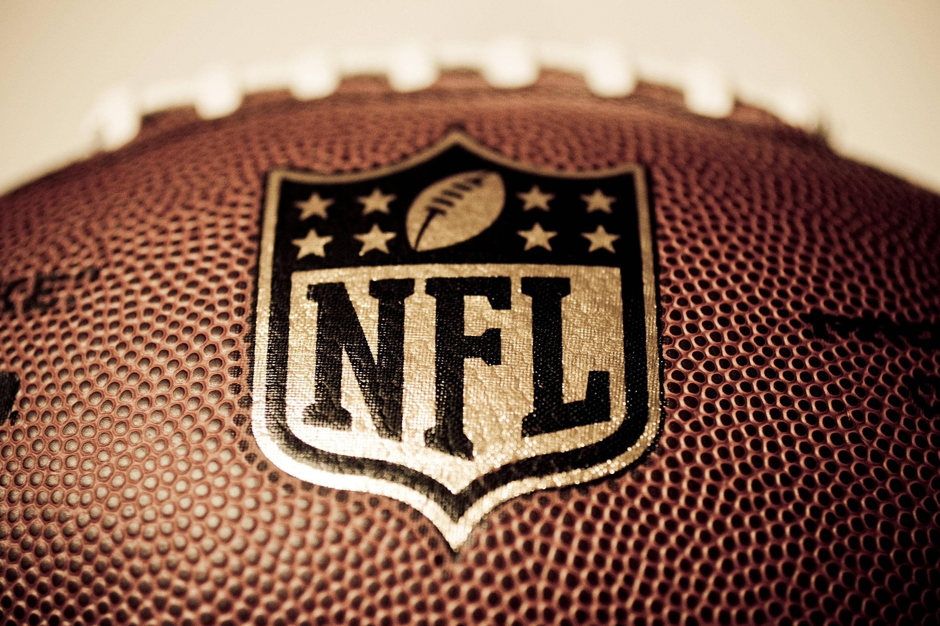 NFL美式足球特寫 壁紙 — NFL 美式足球特寫，帶有紋理皮革和標誌性標誌，呈現溫暖的棕褐色調。