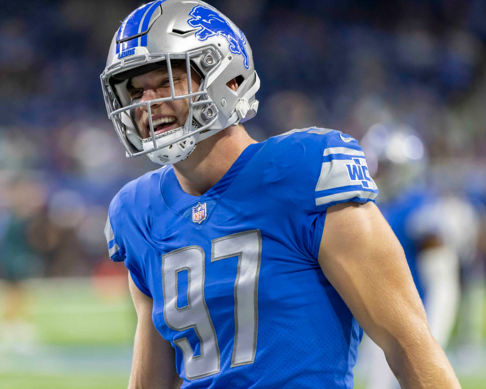 NFL艾丹·漢遜對戰芝加哥熊隊 壁紙 — 一位身穿藍銀裝備的底特律雄獅美式足球員在球場燈光下比賽時大笑。