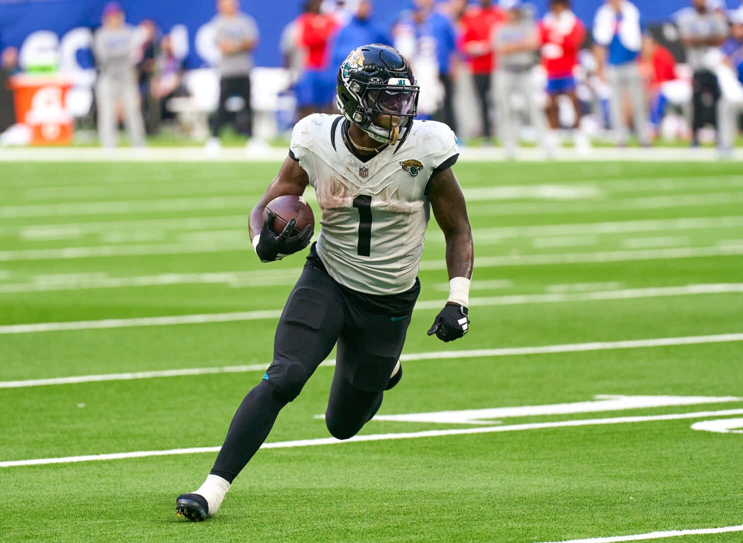 NFL跑衛比賽瞬間 壁紙 — 一名身穿白色球衣的足球運動員在日間比賽中，抱著球在充滿活力的綠色球場上衝刺。
