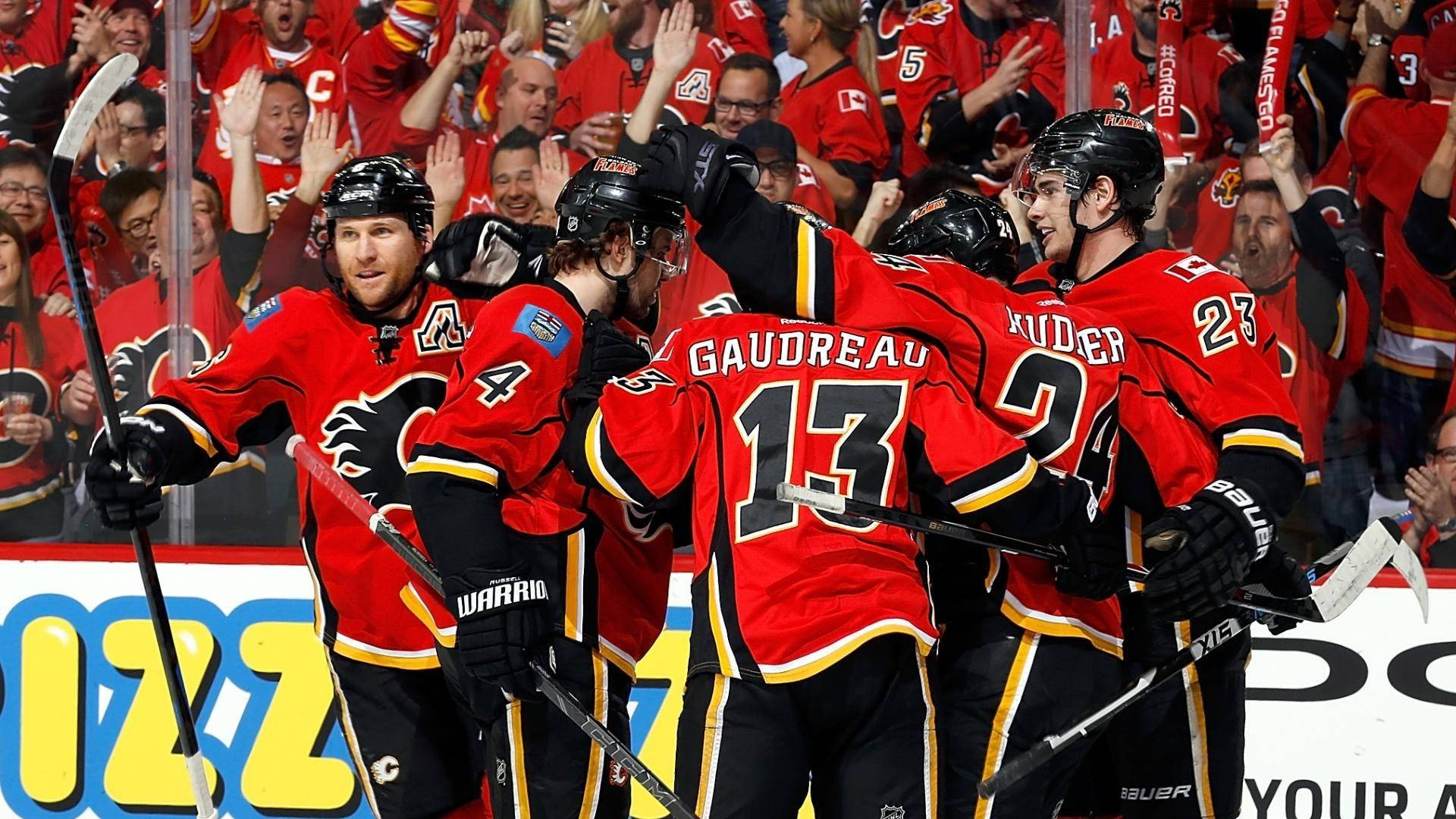 NHL冰球：卡爾加里火焰隊約翰尼·高德魯與隊友 壁紙 — 身穿紅色球衣的曲棍球球員慶祝入球，背景有球迷歡呼。