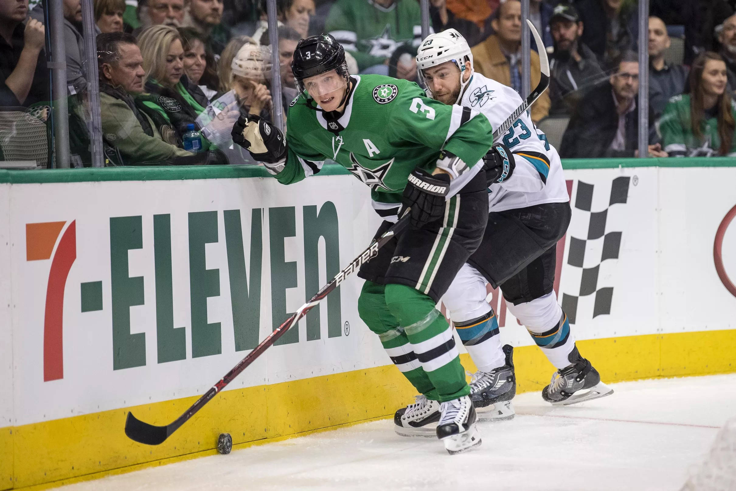 約翰·克林格伯格達拉斯星隊NHL比賽 壁紙 — 兩名曲棍球球員在擠滿觀眾的場館比賽中，沿著板牆激烈爭奪冰球。