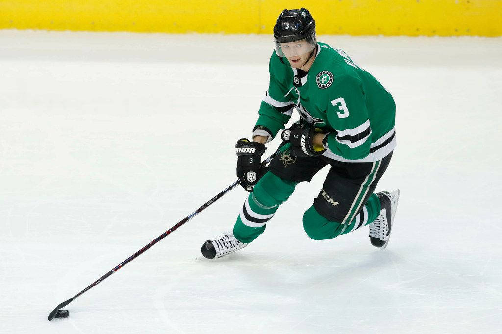 約翰·克林格伯格 NHL 球員海報照 壁紙 — 一名身穿綠色球衣三號的冰球運動員在冰上低身滑行，專注於控球技巧。