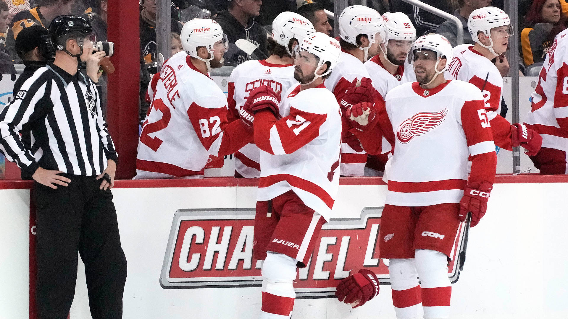 NHL底特律紅翼隊隊長迪倫·拉金 壁紙 — 身穿紅白球衣的冰球運動員在冰場圍板附近慶祝，一名裁判在附近觀察。