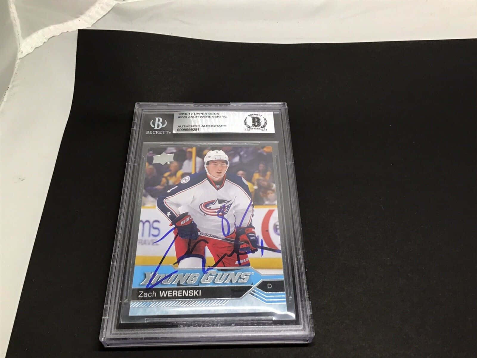NHL新星扎卡里·韋倫斯基親筆簽名高解析度照片 壁紙 — 一張有簽名的 Zach Werenski 曲棍球交易卡放在透明 Beckett 保護殼中，置於黑色表面上，背景有白色布料。