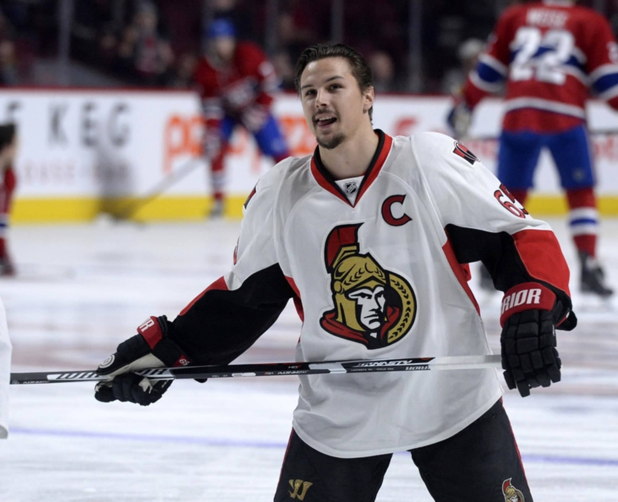 NHL超級明星埃里克·卡爾松動態表現 壁紙 — 一名穿著白色渥太華參議員隊球衣、帶有隊長 'C' 標誌的冰球運動員在比賽期間在冰上慶祝。