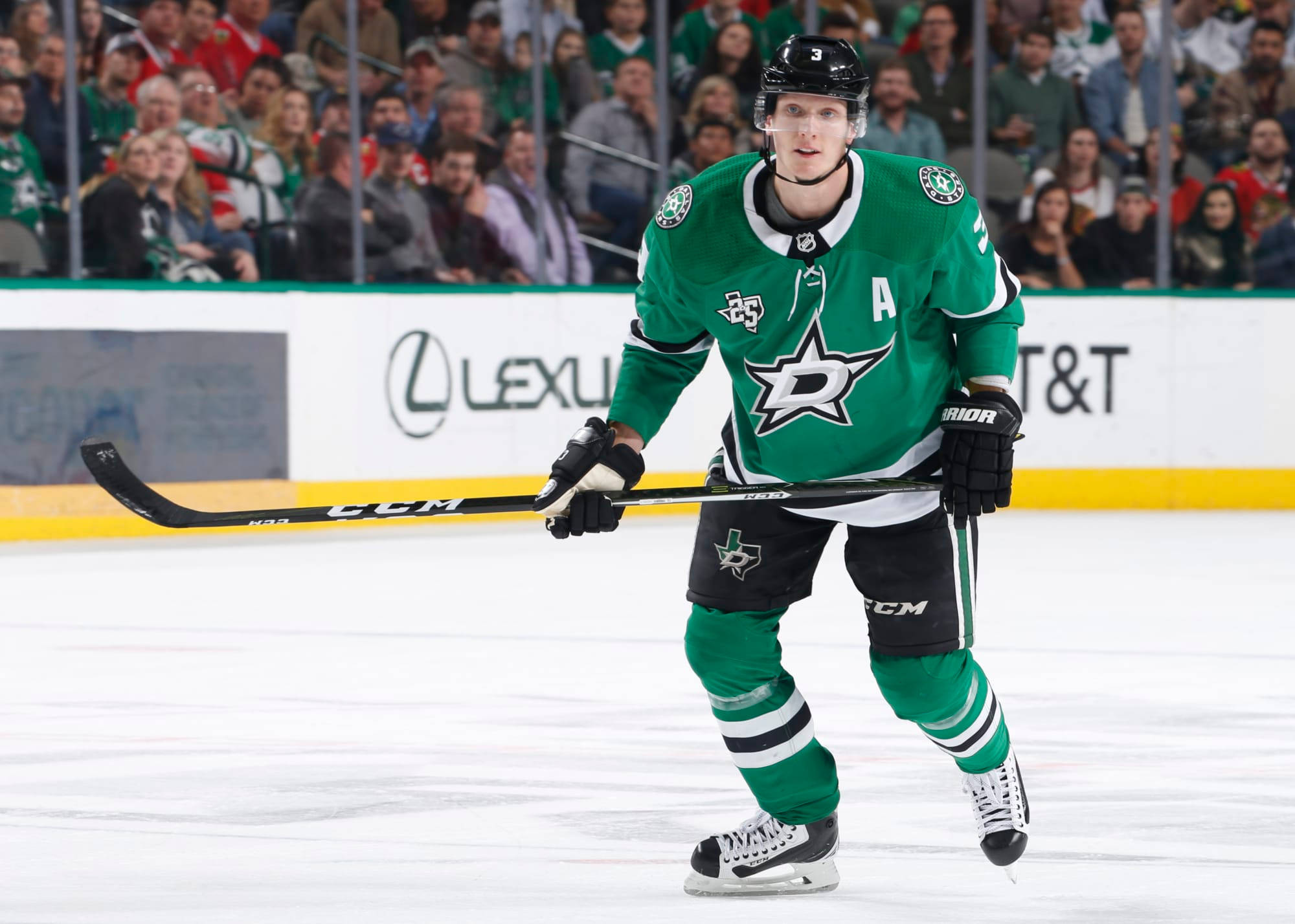 約翰·克林格伯格 達拉斯星隊 NHL 球員 壁紙 — 達拉斯星隊的綠色球衣冰球運動員在比賽中持桿在冰上滑行，背景有觀眾。