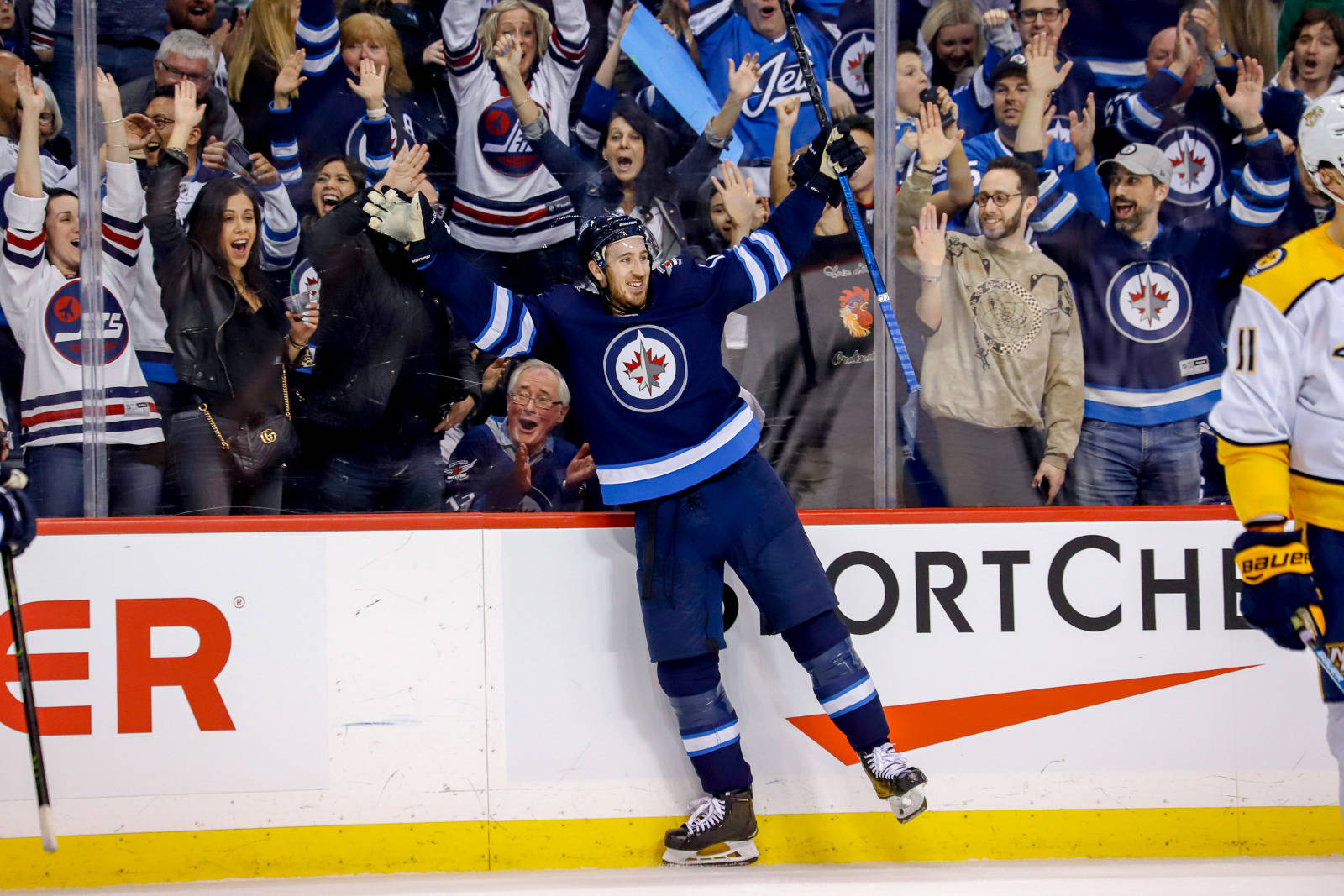 NHL 凱文·海耶斯 紐約遊騎兵隊 壁紙 — 一位欣喜若狂的溫尼伯噴射機冰球球員跳向冰場圍欄，身後穿著藍色球衣的球迷們瘋狂歡呼。