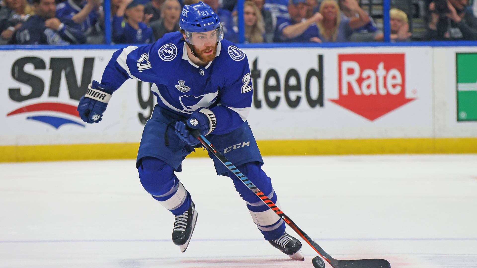 NHL 布雷登·波因特 冰球中鋒 壁紙 — 一名身穿藍色球衣的冰球運動員在冰上激烈滑行，背景有觀眾。