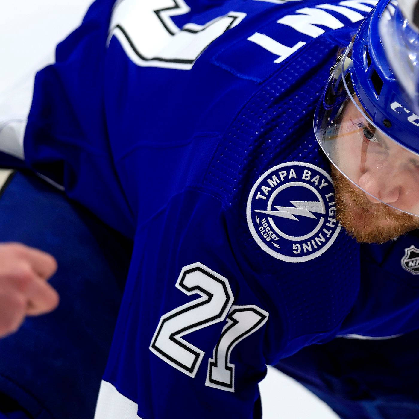 NHL 布雷登·波因特 藍色球衣 壁紙 — 坦帕灣閃電隊冰球球員身穿藍色27號球衣，蹲在冰上，神情專注的特寫。