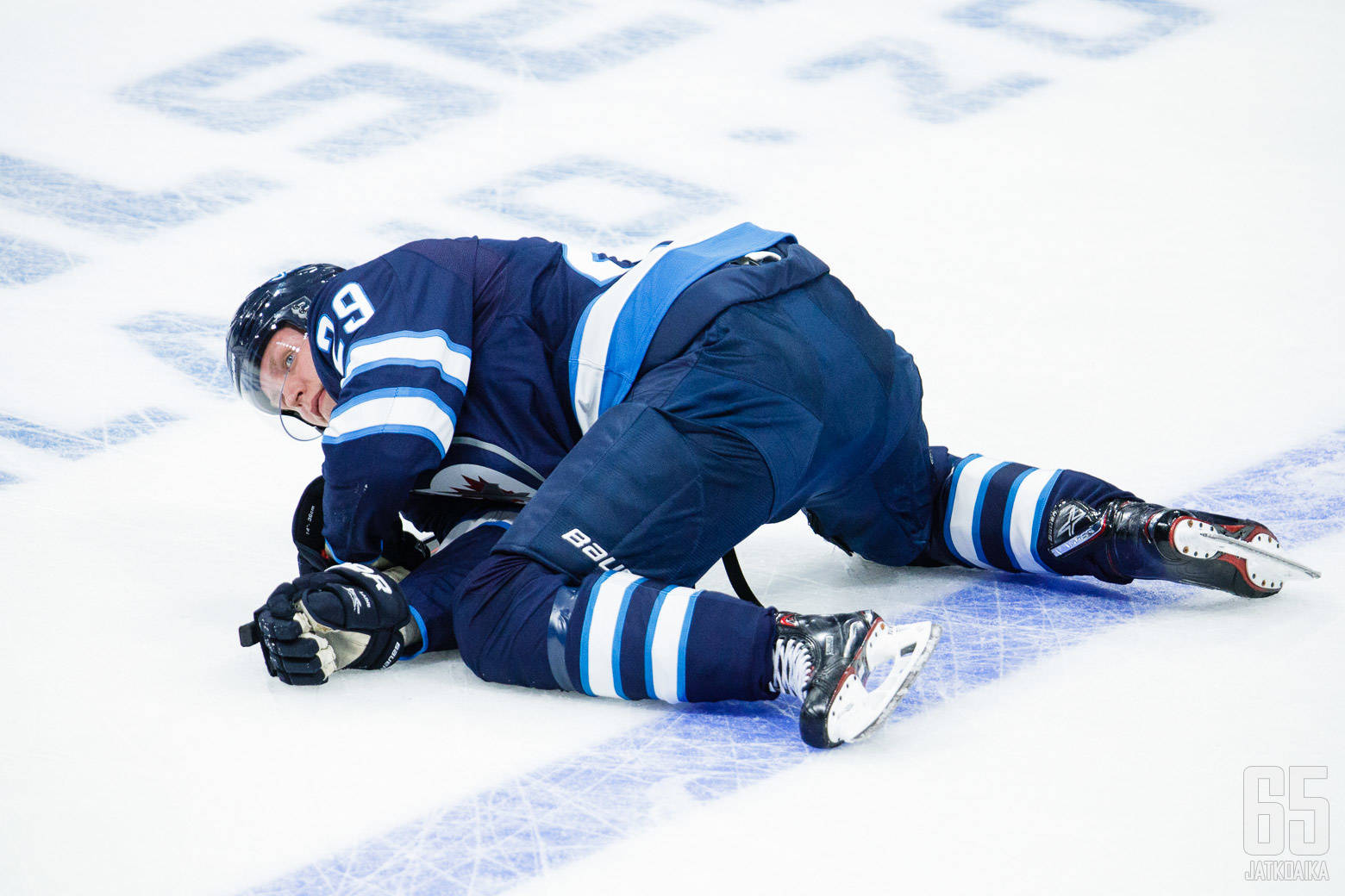 NHL冰球運動員帕特里克·萊恩 壁紙 — 一名身穿藍白球衣的冰球運動員在激烈的比賽中跌倒在冰場上。