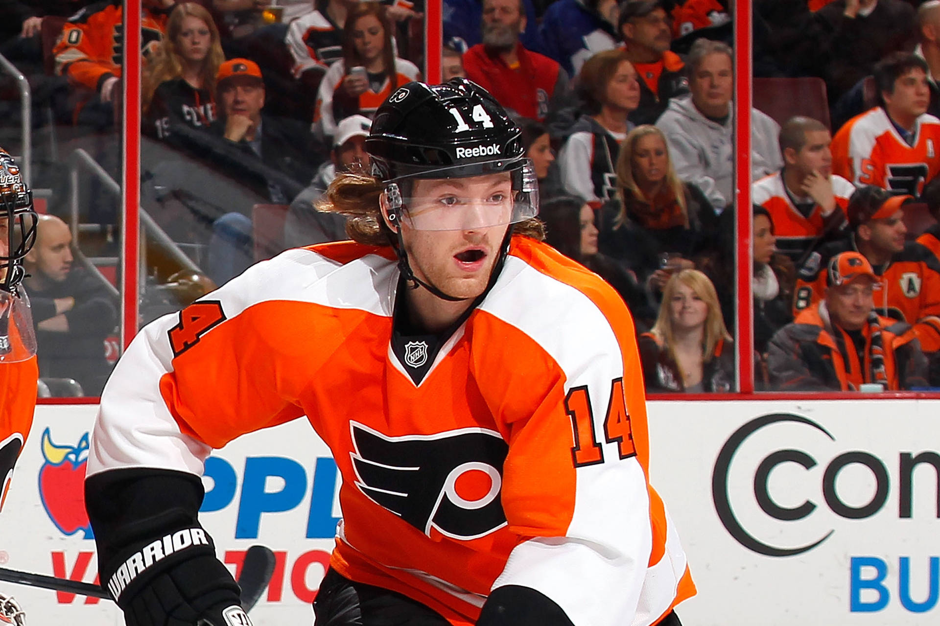 NHL明星賽恩·庫圖爾賽場風采 壁紙 — 一位專注的冰球運動員身穿橙色和白色球衣14號，在比賽中於冰上向前傾，背景有觀眾。
