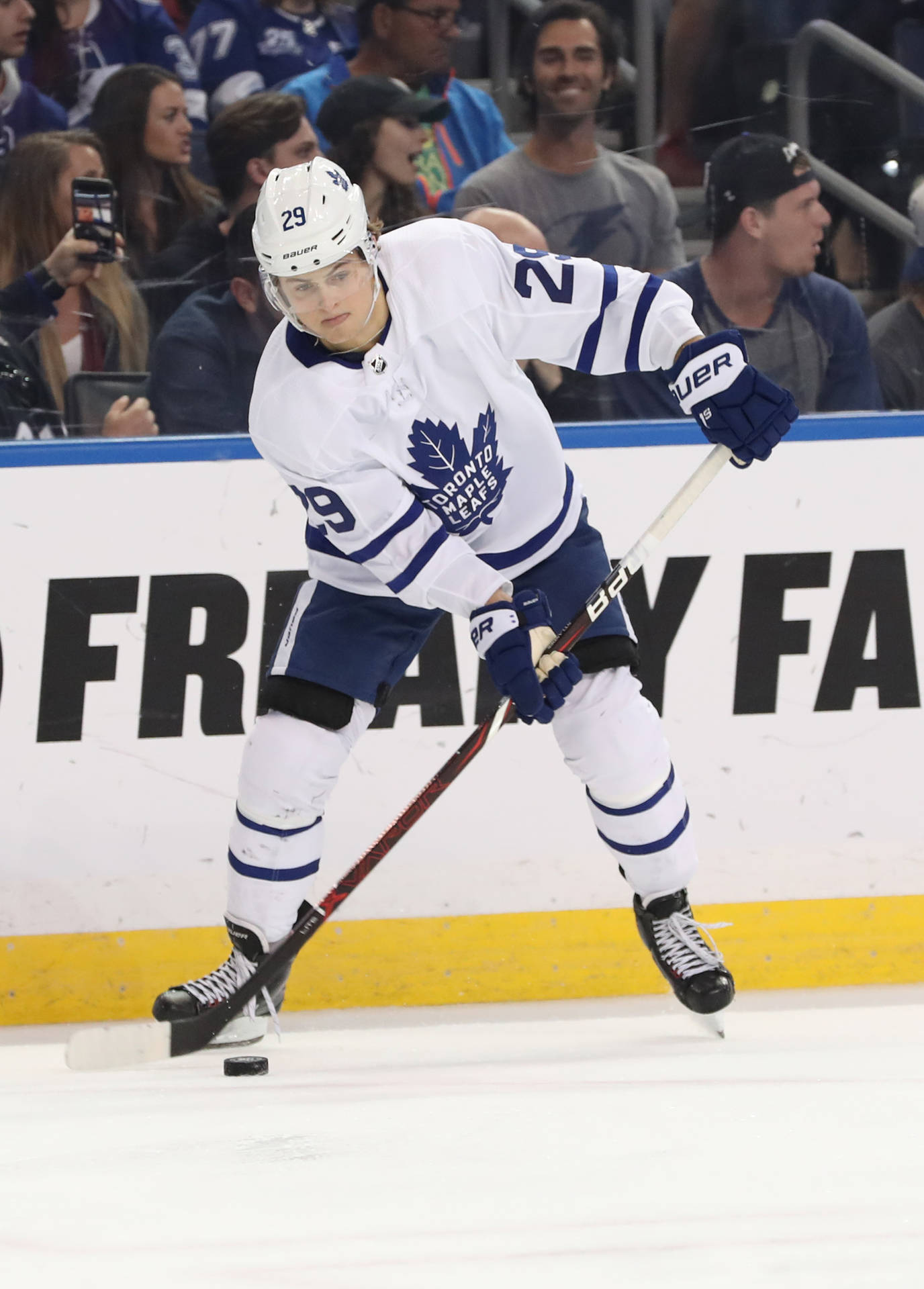NHL球星威廉·尼蘭德動態肖像 壁紙 — 多倫多楓葉隊冰球運動員身穿白色和藍色裝備，在比賽中帶著冰球在冰上激烈滑行。