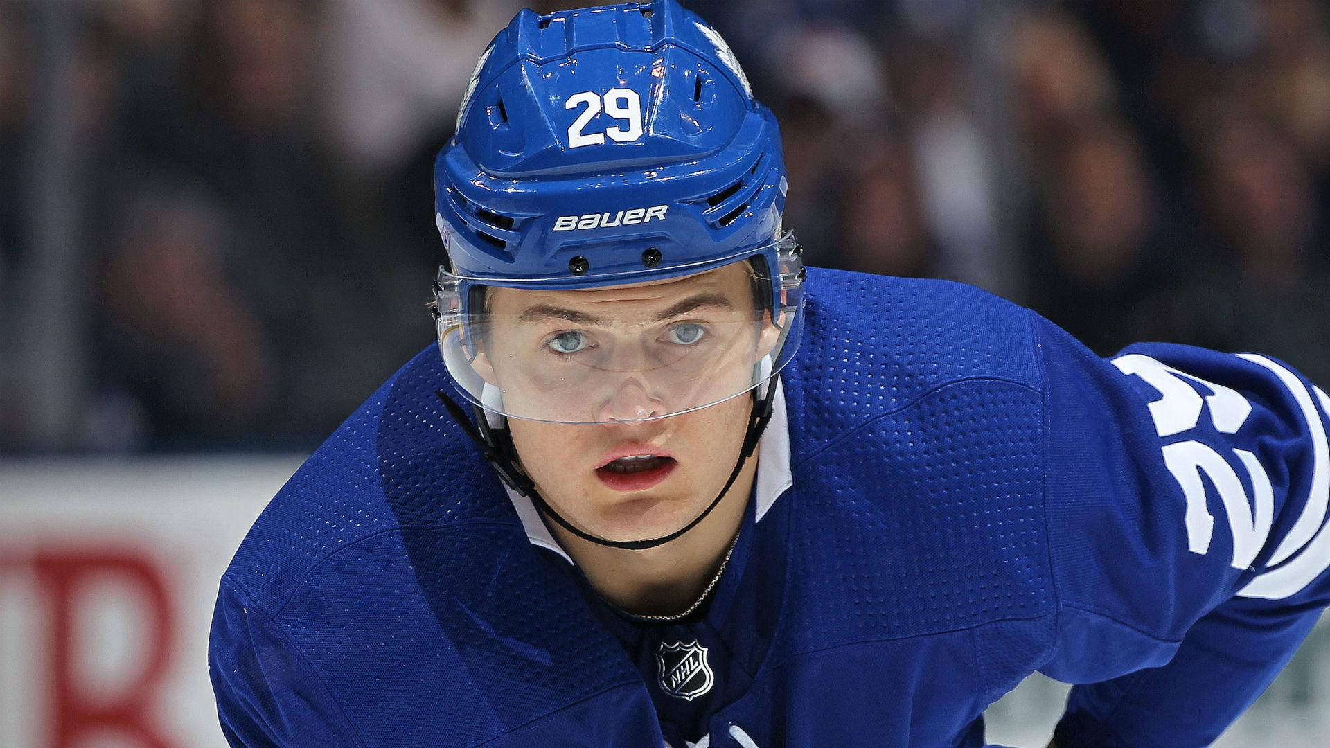 NHL球星威廉·尼蘭德自然瞬間照 壁紙 — 一名專注的冰球運動員身穿藍色球衣和頭盔，在比賽中於冰上向前傾，背景是模糊的觀眾。
