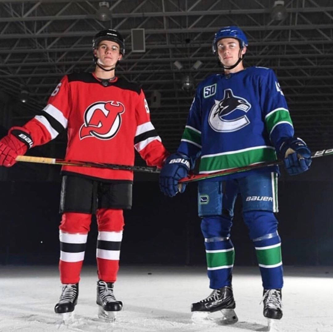 兩名身穿對賽球隊球衣的年輕曲棍球運動員站在冰上手持球棍。