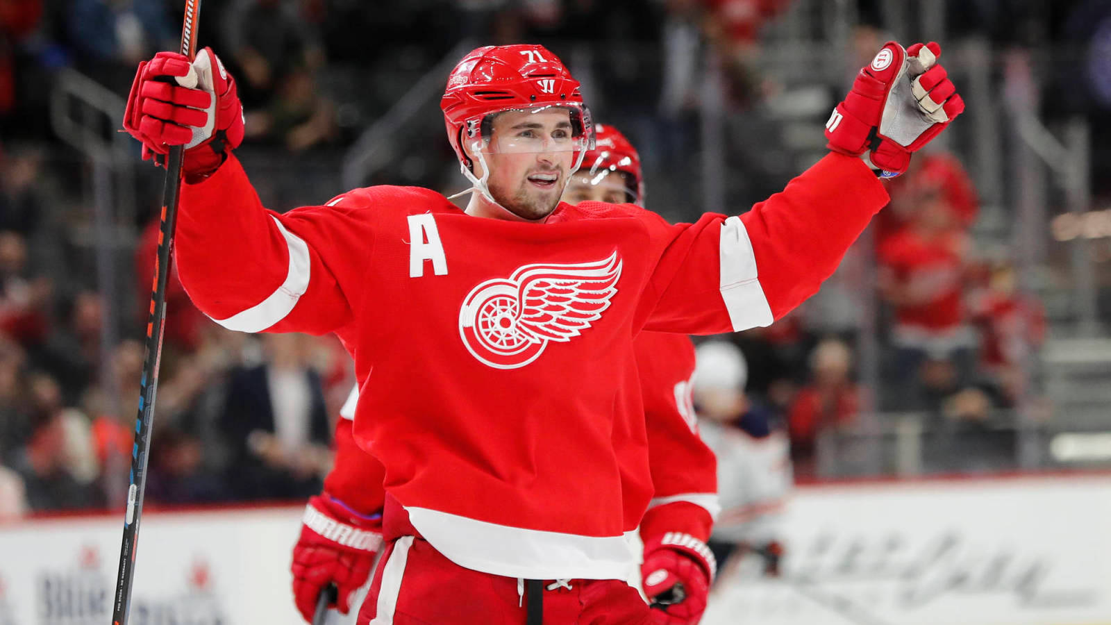 NHL球隊隊長迪倫·拉金 壁紙 — 一位身穿紅色球衣的底特律紅翼冰球球員在冰上高舉球棍慶祝。