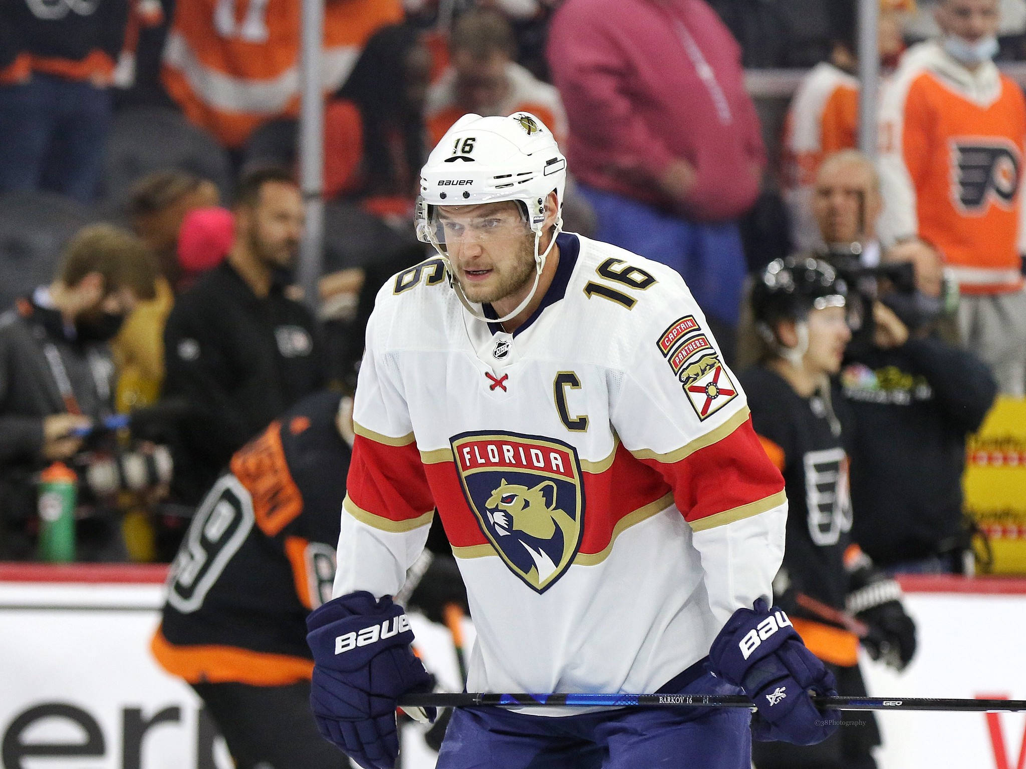 NHL隊長亞歷山大·巴爾科夫對戰費城飛人隊 壁紙 — 一位身穿白色、紅色和金色球衣的佛羅里達黑豹隊冰球隊長在比賽中手持球桿站在冰上，背景有球迷。