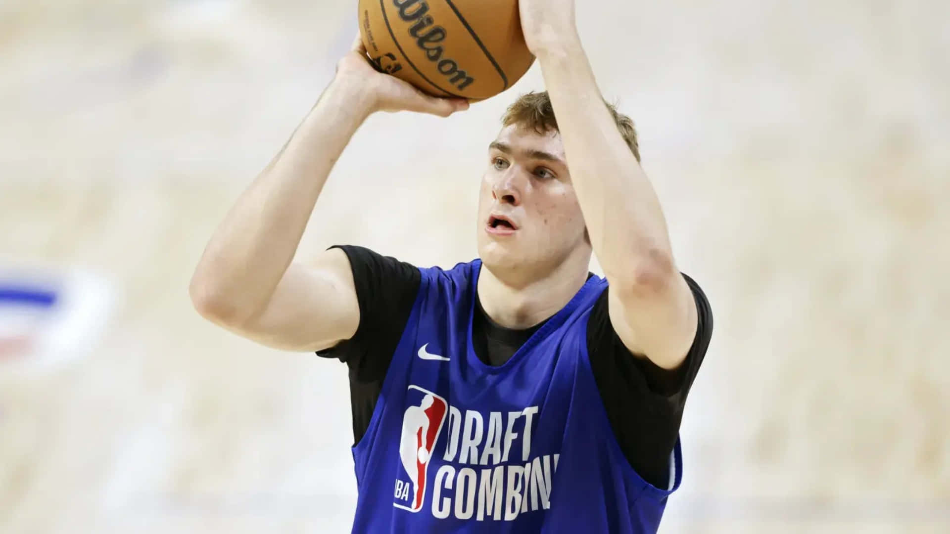  壁紙 — 一位身穿藍色選秀聯合試訓球衣的年輕籃球運動員，正準備以高度專注力投出威爾遜籃球。