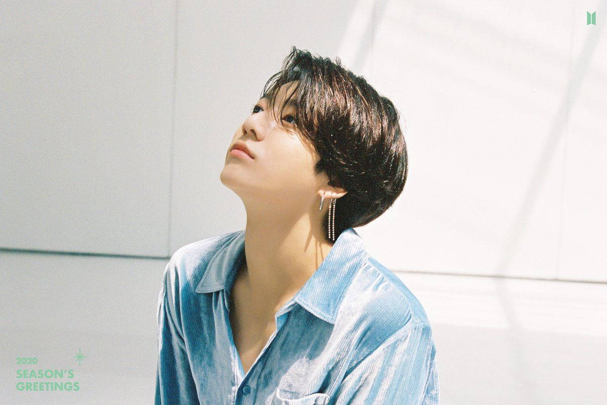 BTS 田柾國 2020 壁紙 — 一位短黑髮、戴著垂墜耳環的年輕男性，在陽光普照的簡約白色空間中穿著藍色條紋襯衫向上凝視。