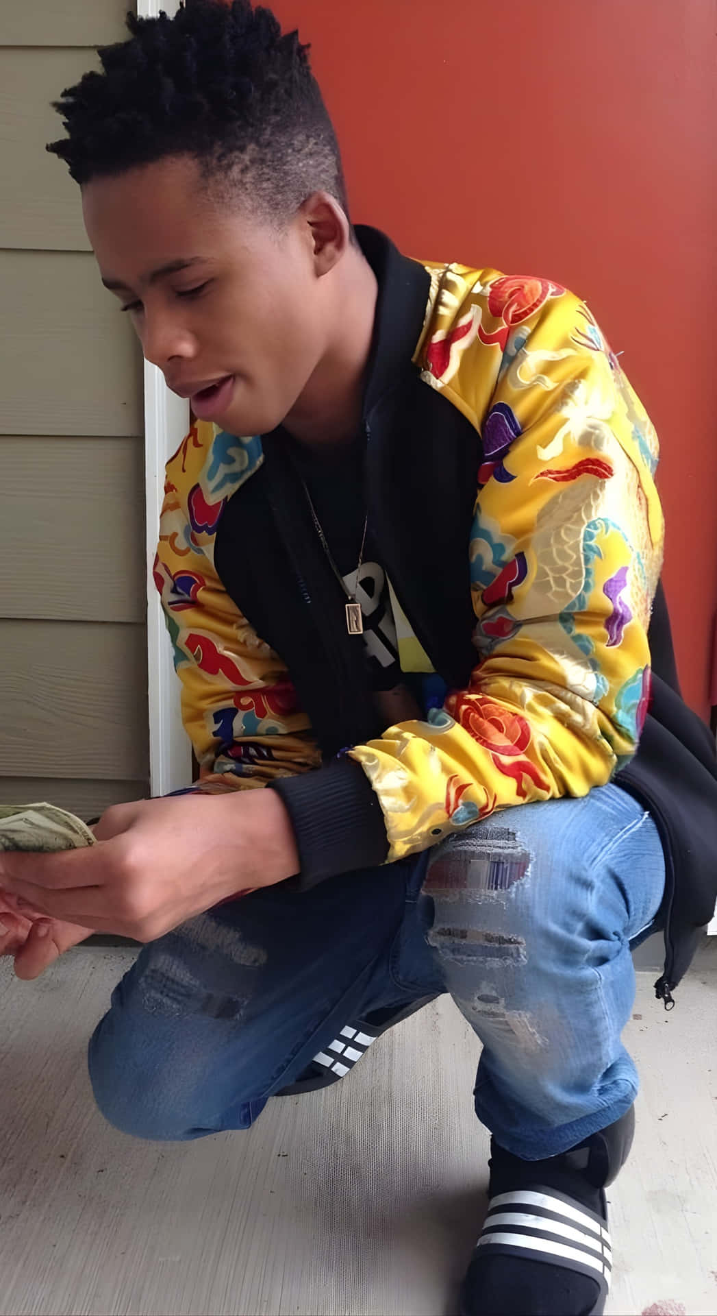  壁紙 — 一名身穿鮮黃色龍紋外套的年輕男子蹲在室內，神情專注地數錢。