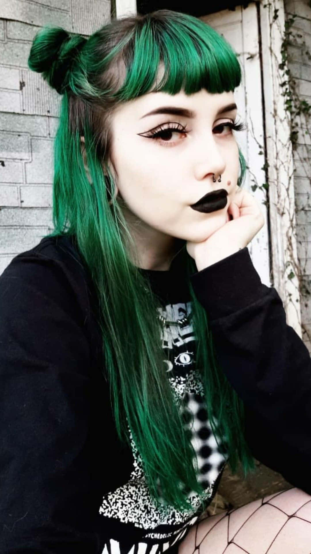  壁紙 — 一位年輕女性，擁有鮮綠色頭髮梳成髮髻，搭配大膽的黑色妝容，在風化的磚牆前若有所思地擺姿勢。
