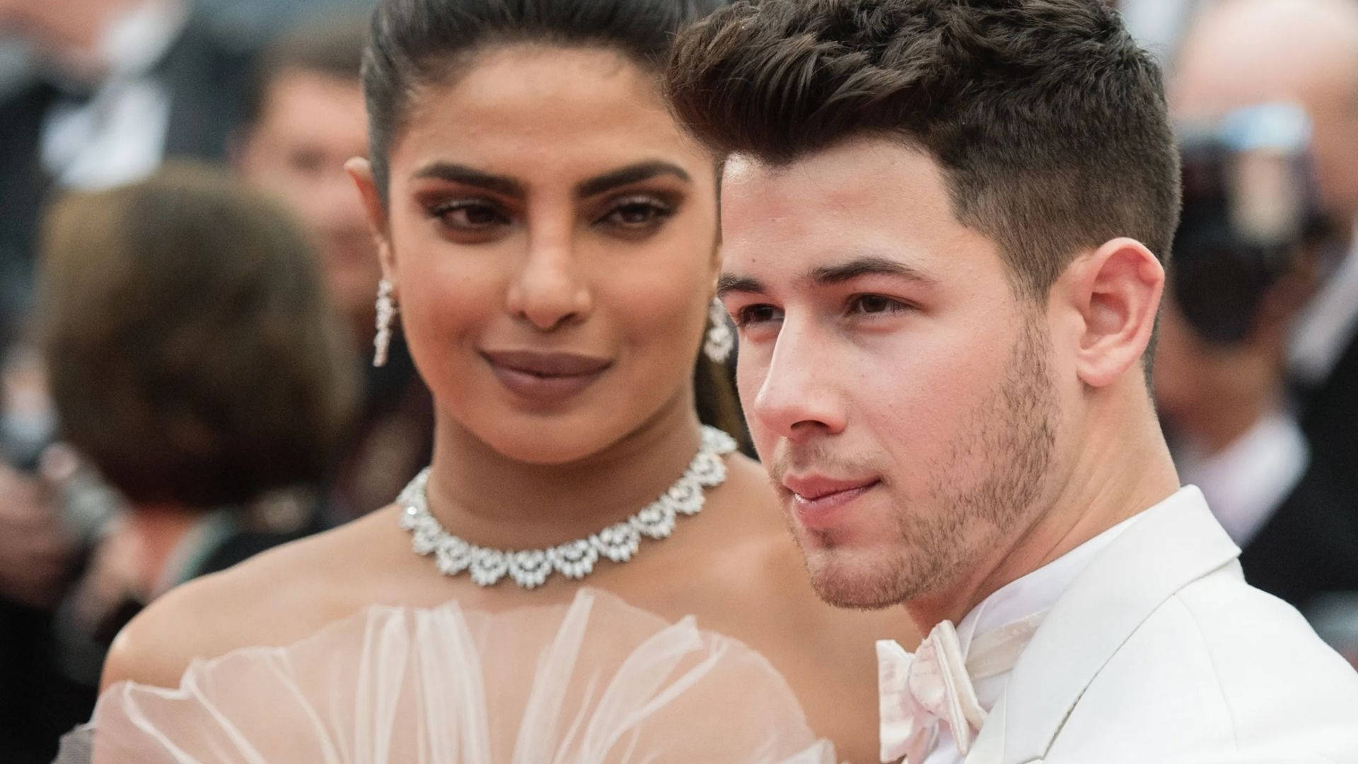 Nick Jonas 的妻子 Priyanka Chopra 壁紙 — 一對穿著白色正裝的迷人夫婦在紅地毯活動上緊密擺姿勢，背景有閃爍的相機。