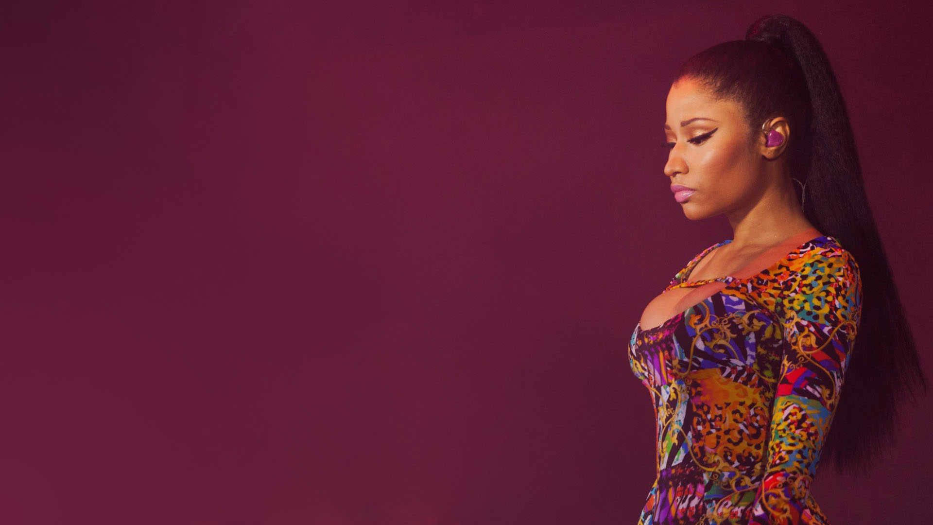 Nicki Minaj 熱情演出 壁紙 — 一位身穿鮮豔圖案連衣裙的女性側身站在深紫色背景前，目光低垂，靜靜沉思。
