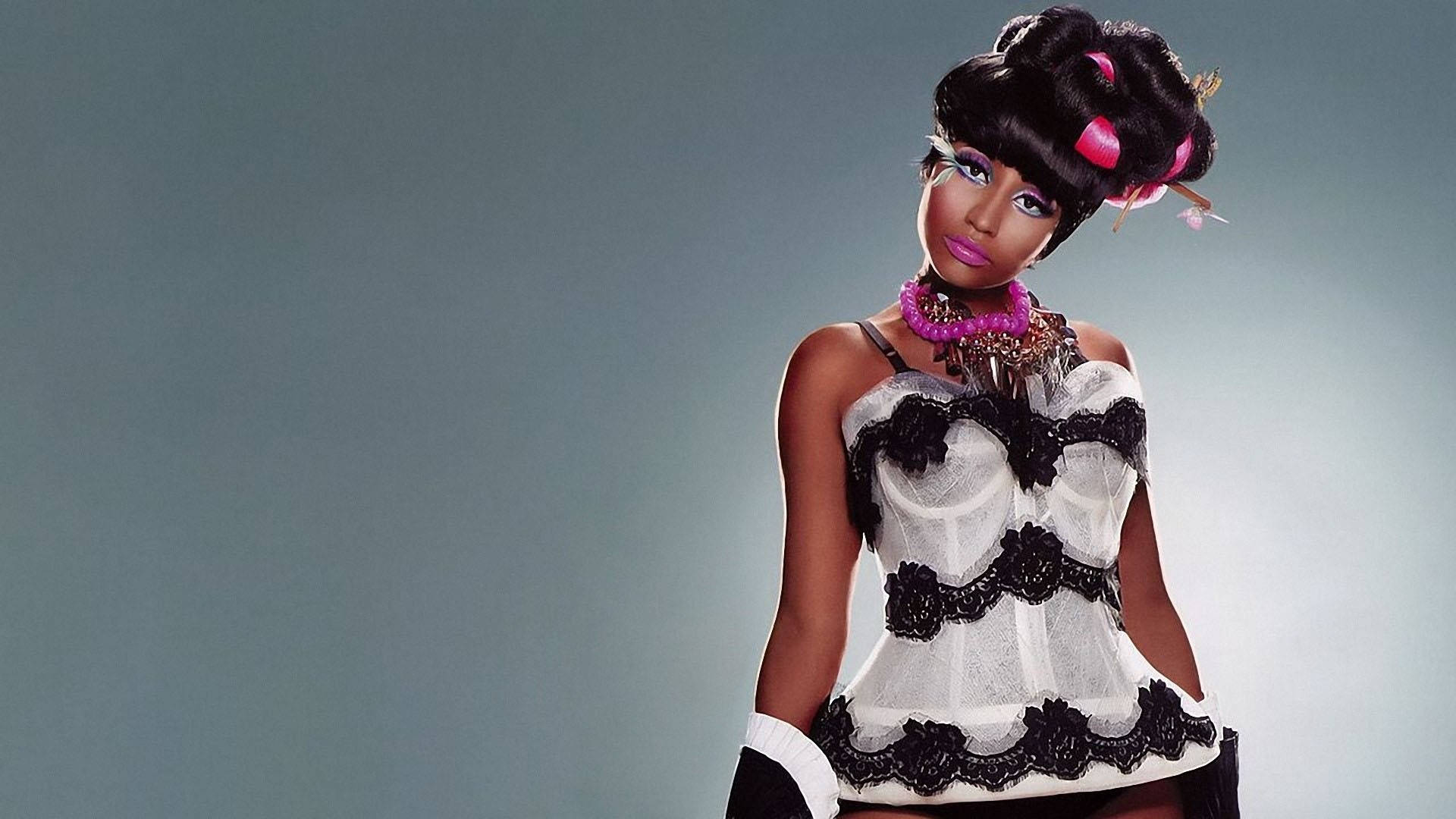 Nicki Minaj 玩偶造型 壁紙 — 一位擁有豐盈黑髮、飾有粉紅色髮捲的女性，在柔和的灰色背景下，自信地穿著黑白蕾絲服裝擺姿勢。