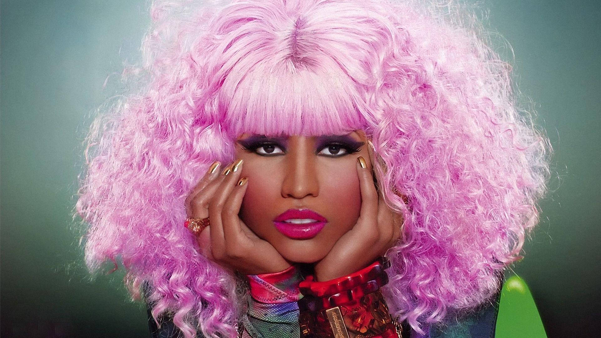 Nicki Minaj 紫色捲髮造型 壁紙 — 一個擁有豐盈粉紅捲髮和大膽妝容的人，在柔和的綠色背景前用手托著臉。