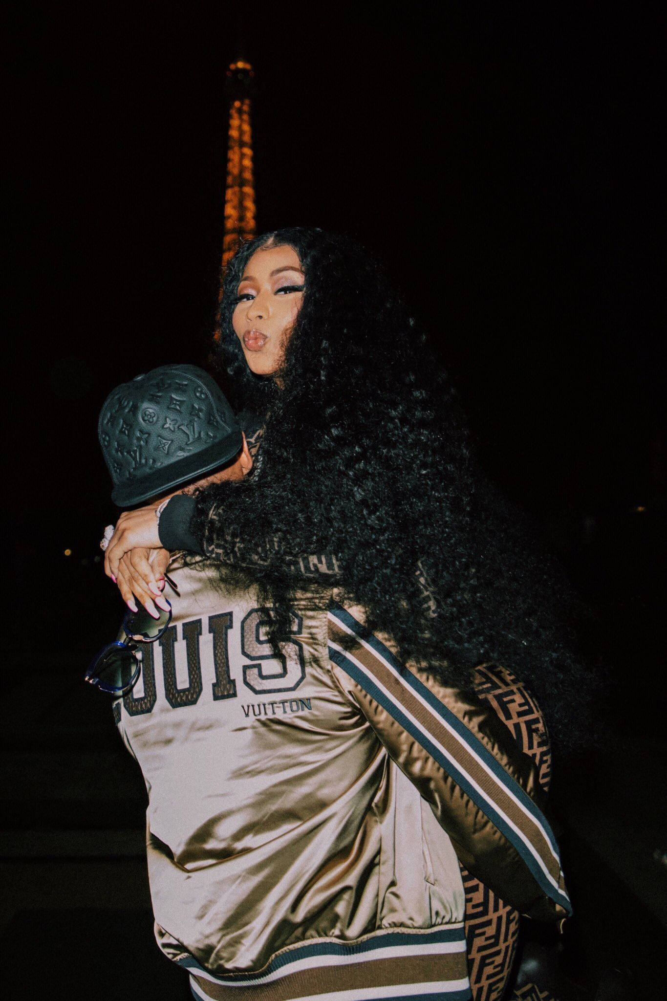 Nicki Minaj 與 Kenneth Petty 壁紙 — 一位擁有黑色長曲髮的女性在夜晚擁抱著一位穿著金色Louis Vuitton外套的人，背景是發光的艾菲爾鐵塔。