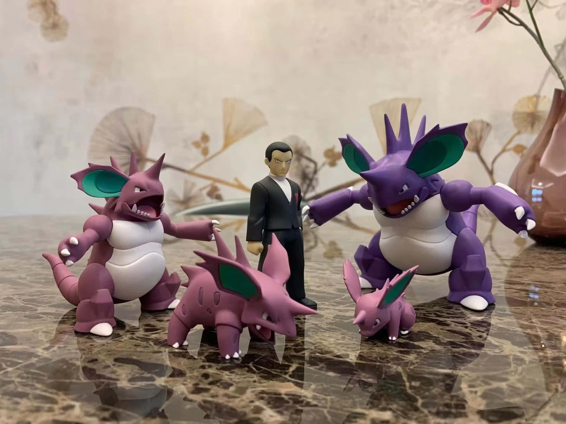 威嚴的Nidoking 於戰鬥中 壁紙 — 四個紫色和白色的 Pokémon 公仔和一個穿西裝的男人站在反光的大理石表面上，背後有花卉牆紙。
