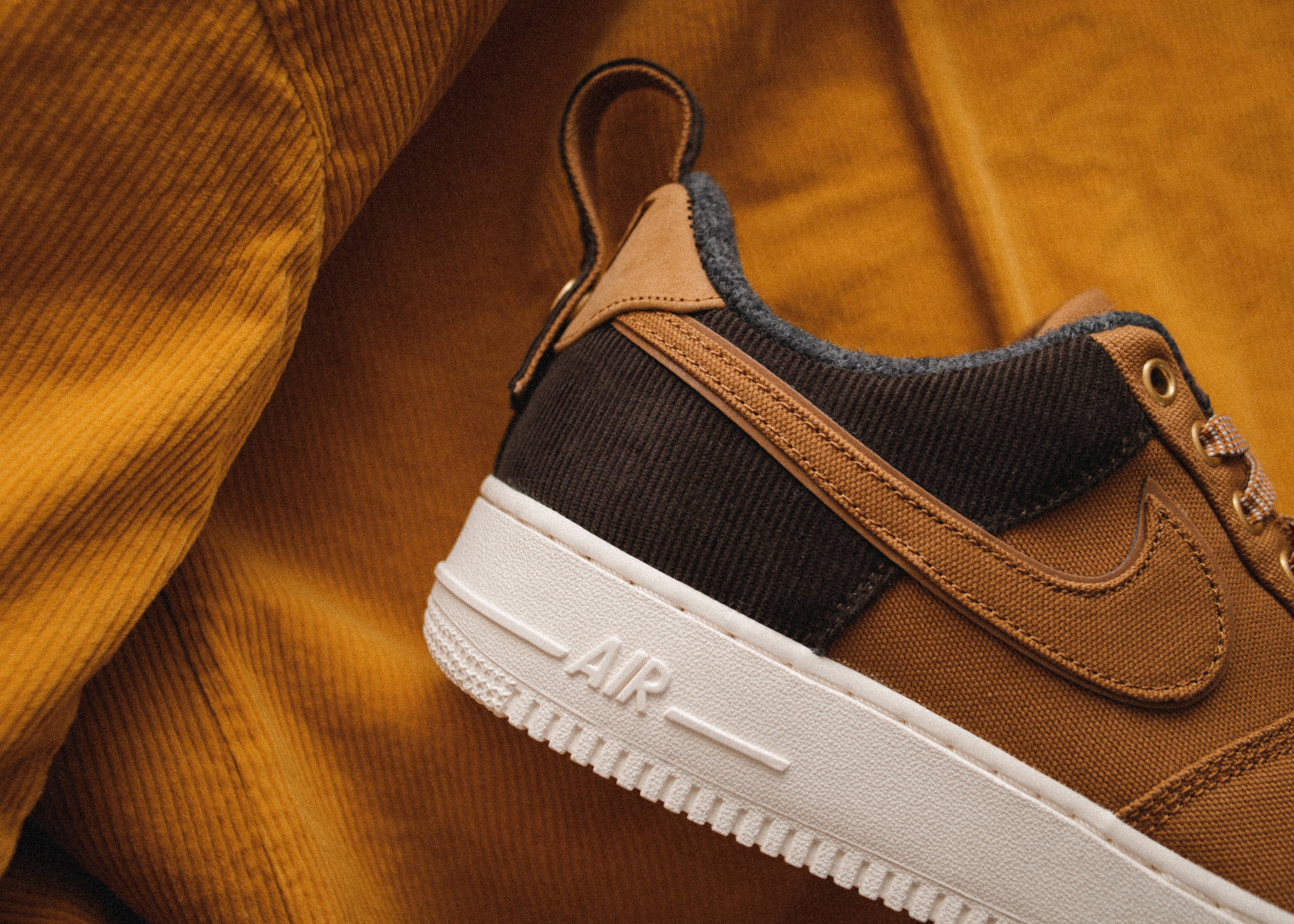 Nike Air Force 1運動鞋 壁紙 — 近距離拍攝一雙棕色Nike Air運動鞋，白色鞋底，置於芥末黃色燈芯絨布料上。