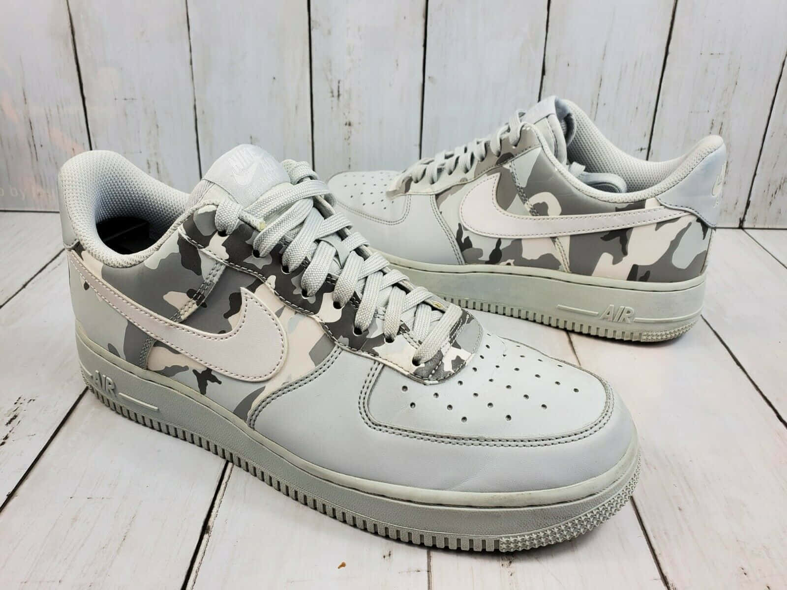 白灰迷彩Nike Air Force 1圖片 壁紙 — 一對灰色迷彩Nike Air Force 1波鞋放在經風化的白色木地板上。