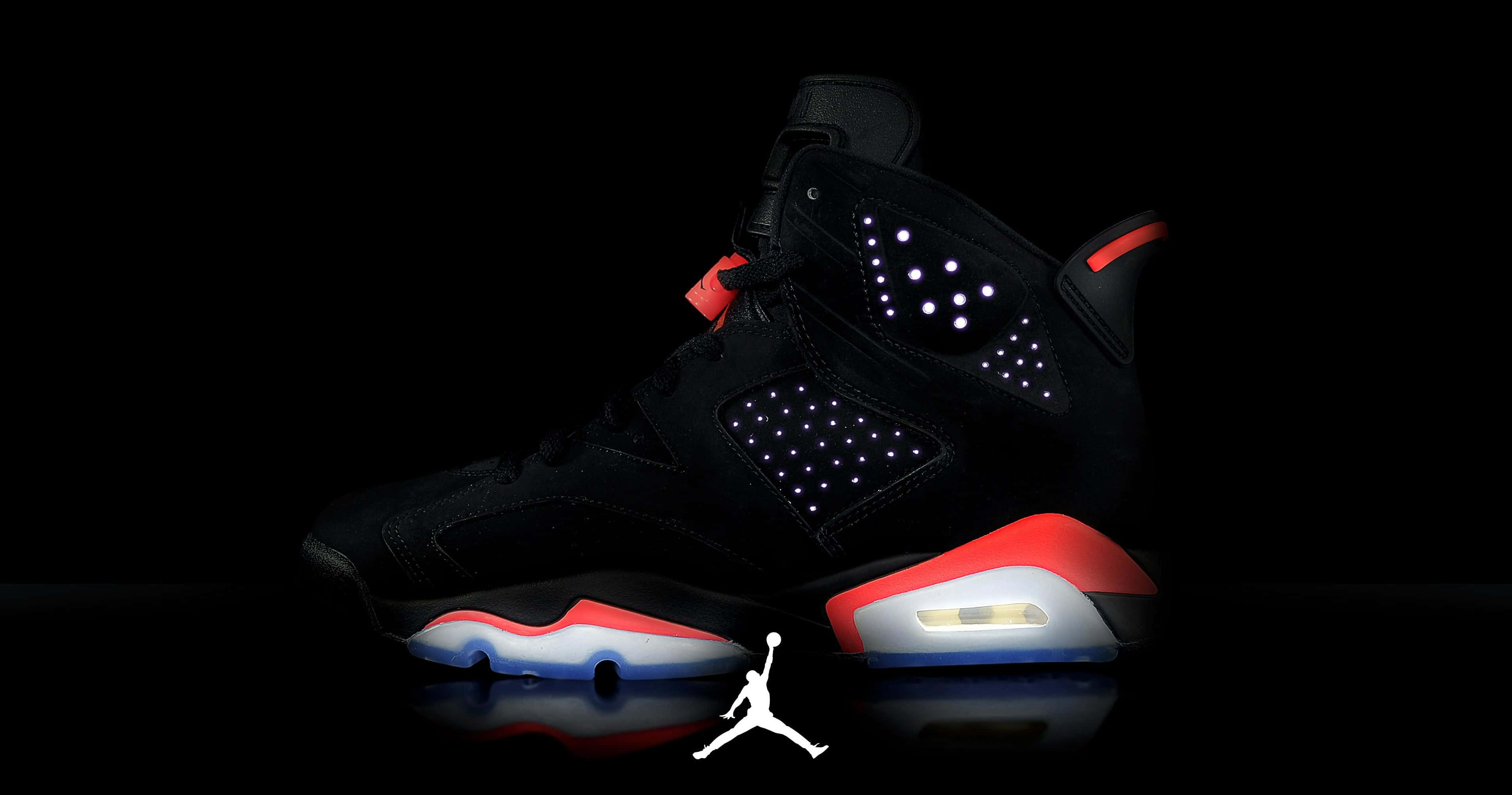 Nike Air Jordan — 夢想成真 壁紙 — 一對黑色Jordan運動鞋，帶有發光的紅色、白色和藍色點綴，孤立地站在反射表面上，背景為漆黑一片。