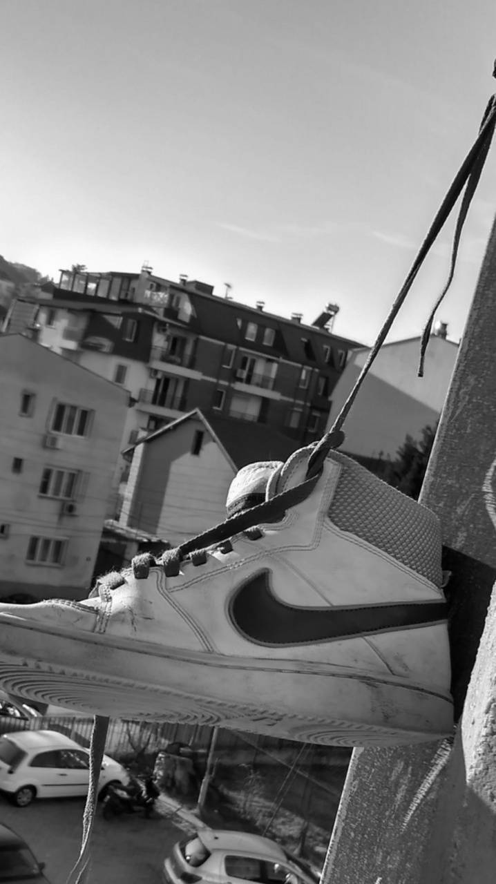 獨特街頭風格的Nike鞋款，時尚現代感十足 壁紙 — 一隻破舊的Nike運動鞋用鞋帶掛在混凝土邊緣上，背景是城市公寓大樓。