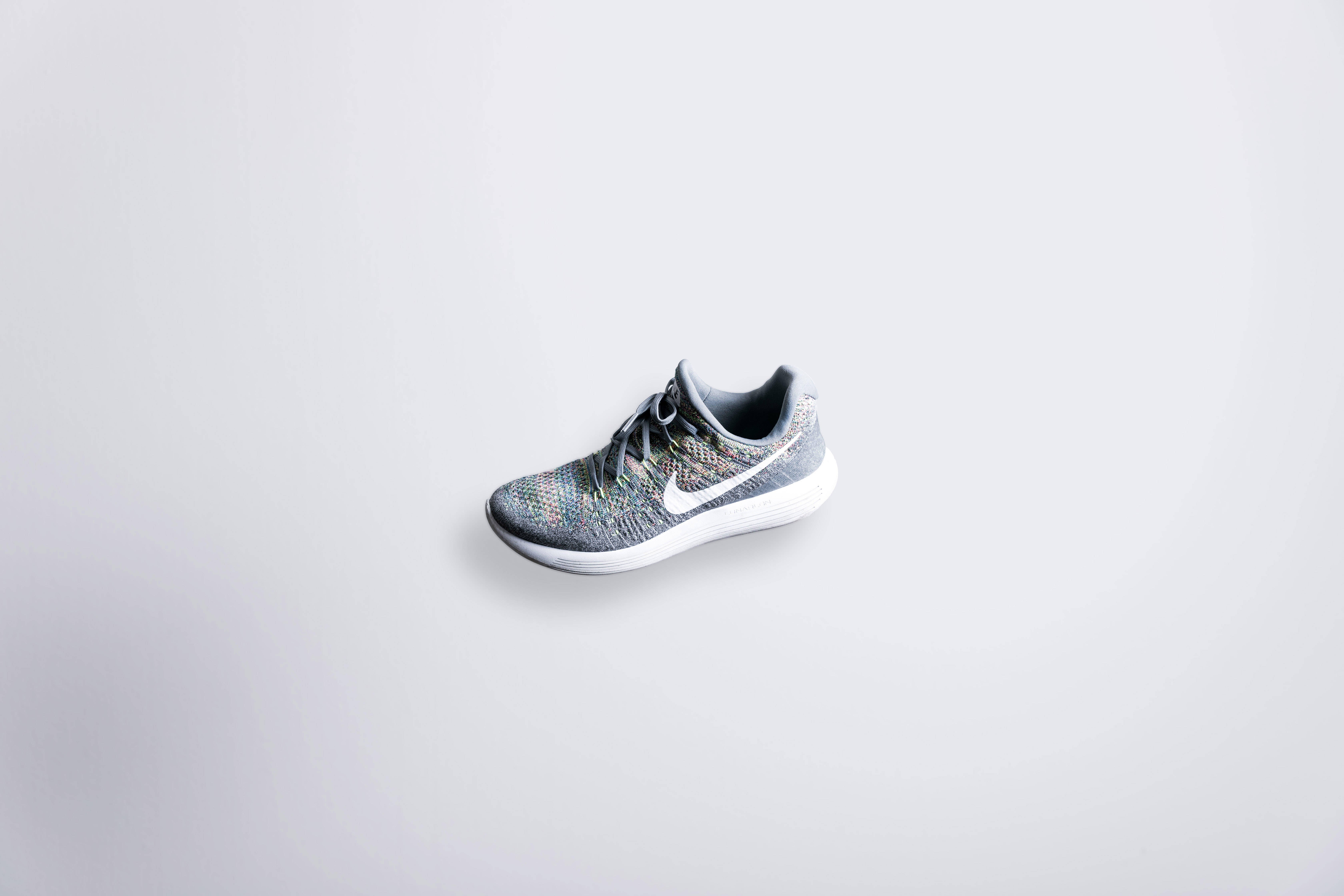 Nike Free Rn Flyknit 運動鞋 壁紙 — 一隻灰色針織跑鞋帶有白色 swoosh，漂浮在極簡的淺灰色背景上。