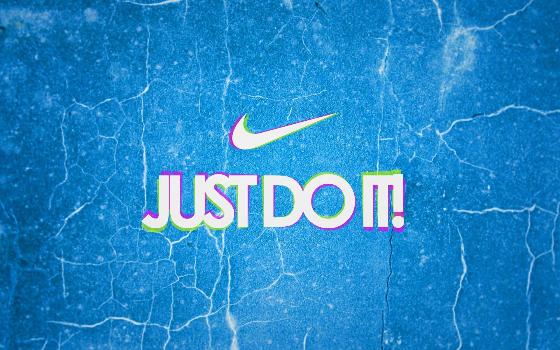 Nike Girl Swoosh標誌 壁紙 — 充滿活力的 Nike 'Just Do It!' 標語，以粗體彩色字體呈現在裂紋藍色紋理背景上。