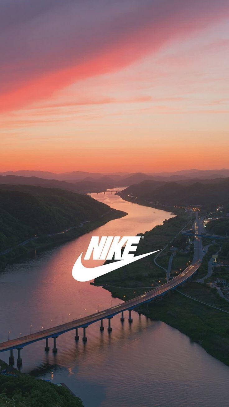 Nike iPhone 橋樑日落背景 壁紙 — 鳥瞰圖：日落時分蜿蜒的河流，橋樑和道路在粉橙色天空下閃耀，並疊加Nike標誌。
