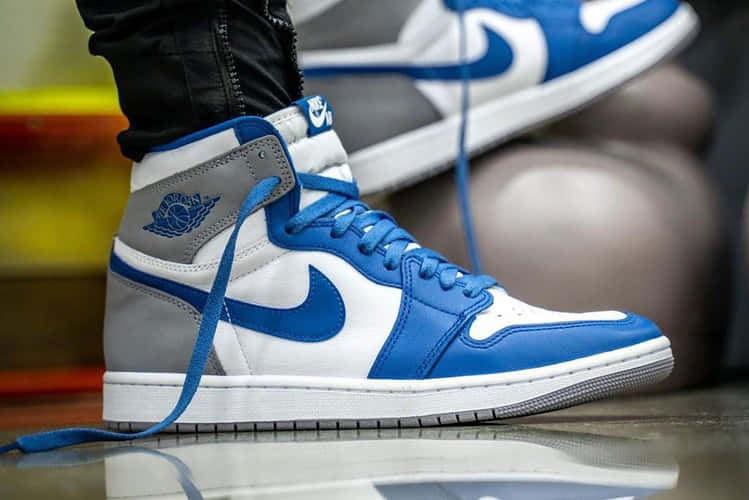 藍白灰色Jordan 1高筒運動鞋，鞋帶未繫，置於反光地板上。