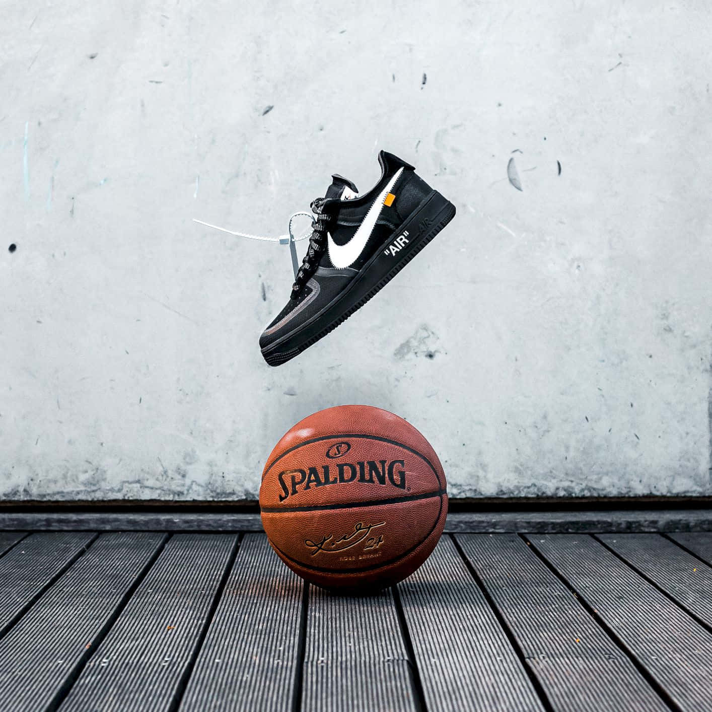 以Nike籃球鞋釋放你的運動潛能 壁紙 — 一對黑色Nike運動鞋懸浮在一個Spalding籃球上方，背景是磨損的木地板和混凝土牆。
