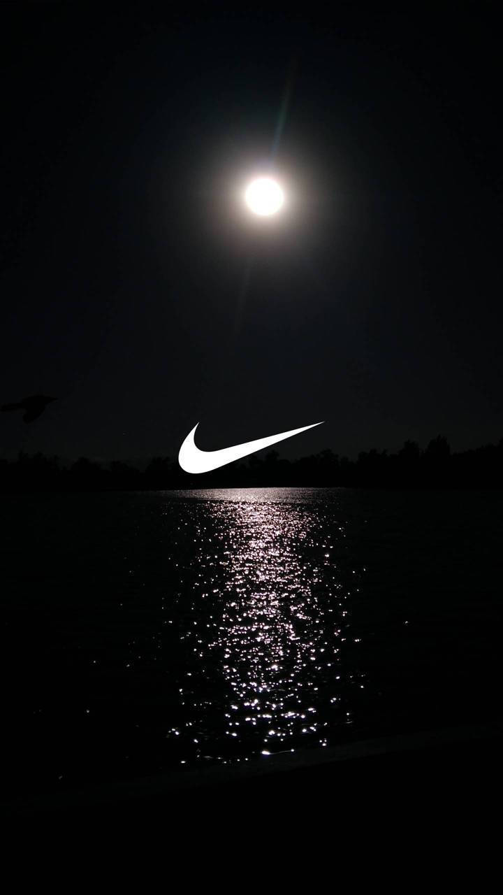 Nike Swoosh夜空圖 壁紙 — 一輪發光的月亮照亮黑暗的湖泊，一個白色Nike勾勾漂浮在閃爍的水面上。