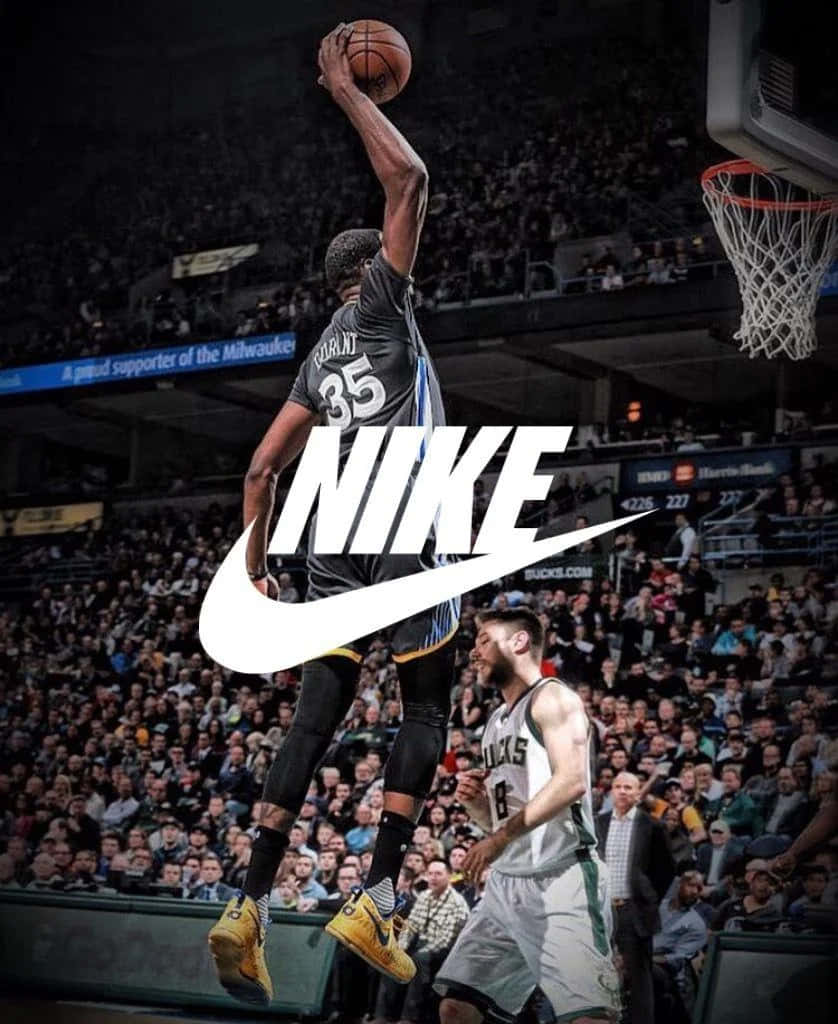 以Nike籃球鞋達成你的極限 壁紙 — 一名身穿密爾沃基公鹿隊球衣的籃球運動員飛身入樽，防守球員在下方觀看，場館內座無虛席。