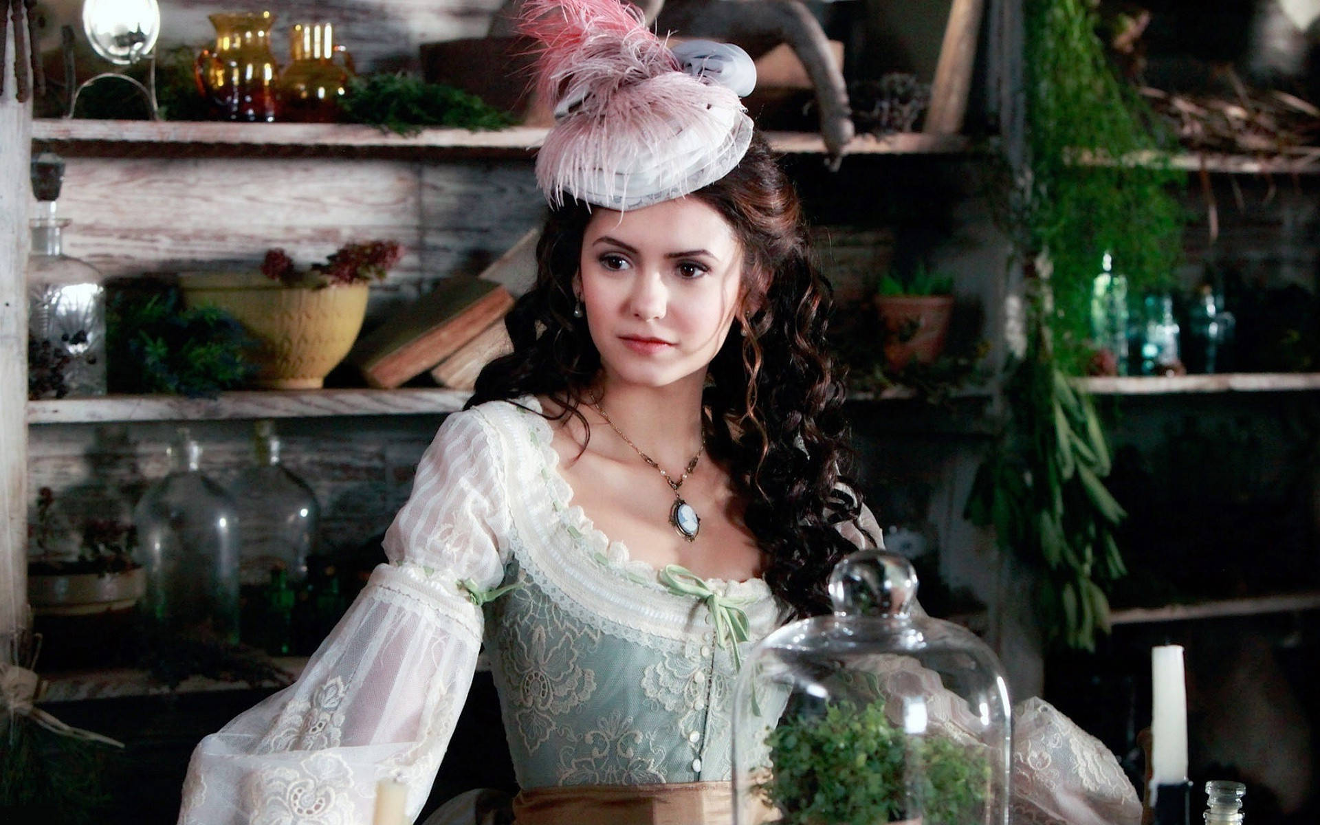 Nina Dobrev 古典連衣裙 壁紙 — 一位穿著復古蕾絲長裙和羽毛帽子的女士站在一個充滿玻璃罐和草藥的鄉村藥房裡。