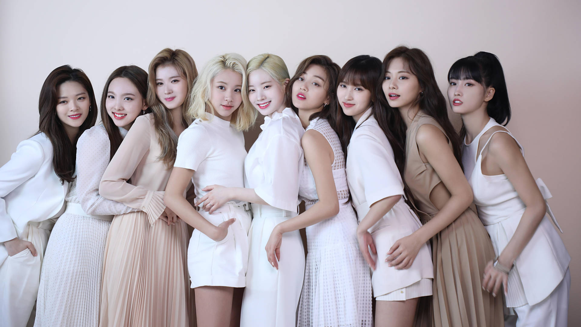 Twice 4K 穿著中性服裝 壁紙 — 九位身穿白色和米色服裝的女性在柔和粉紅色背景和溫暖燈光下緊密地擺姿勢。
