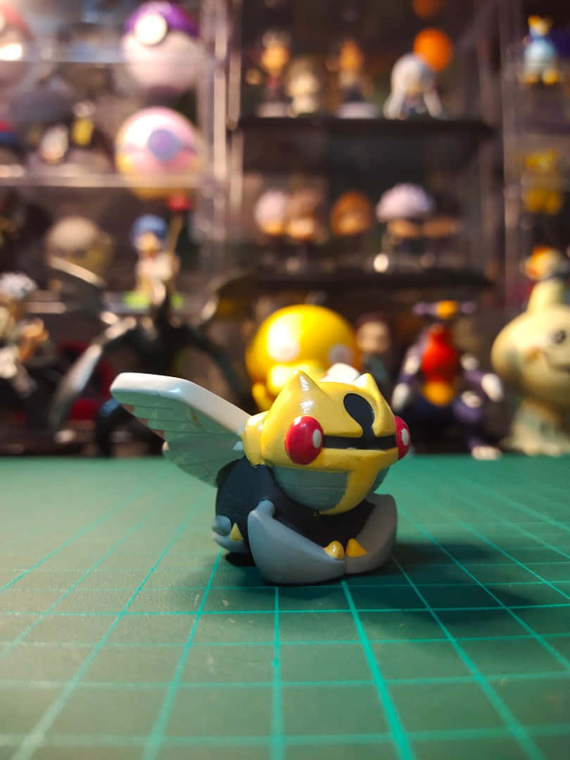 Ninjask 手指玩偶 壁紙 — 一個黃黑色、紅眼睛的寵物小精靈公仔坐在綠色格仔墊上，背景有模糊的其他收藏品貨架。