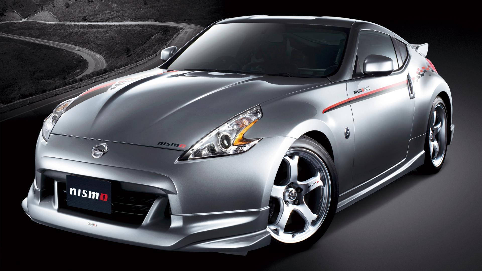 經典運動跑車 — Nissan 350z 壁紙 — 一輛時尚的銀色日產350Z Nismo跑車，帶有紅色點綴和定制輪圈，在黑暗蜿蜒的道路背景下展示。